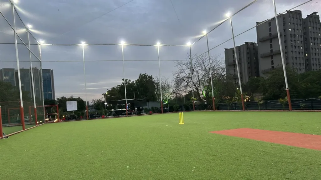 A cricket ground lit by floodlights at dusk with the stumps set on the pitch
