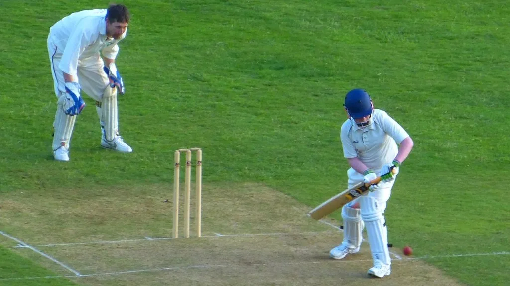 A batter taking guard at the crease with the wicketkeeper standing behind the stumps